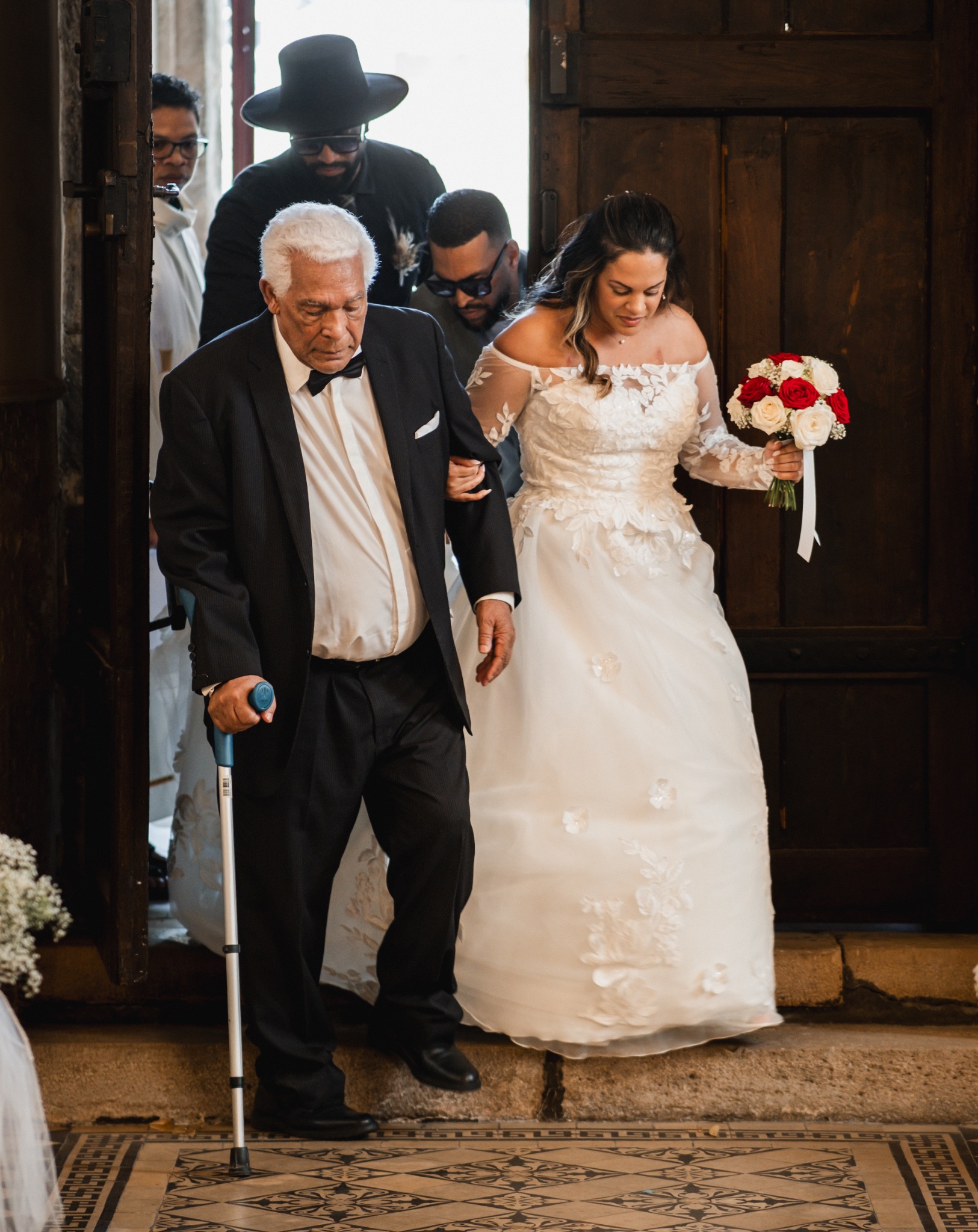 Un homme âgé s'appuyant sur une canne accompagne la mariée à la sortie de l'église